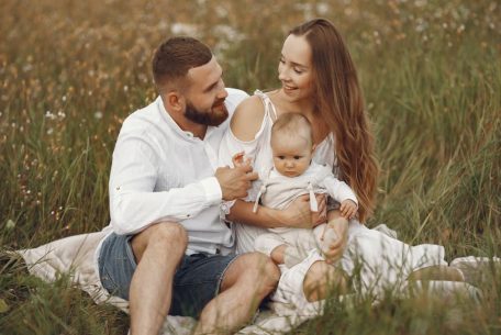 A joyful couple with their baby sitting on a blanket in a sunny meadow, embracing the beauty of summer.